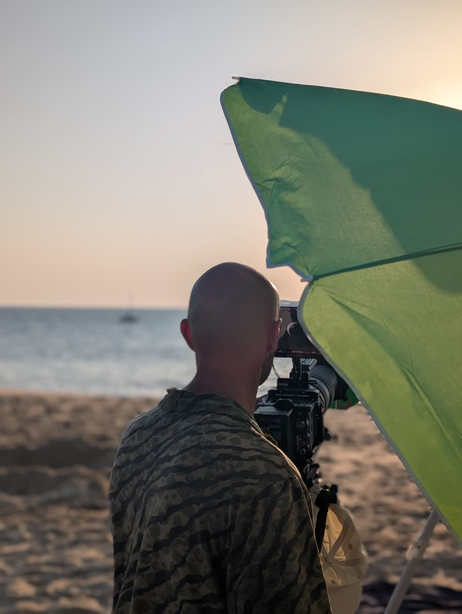 Alexandre Lesbats derrière sa caméra RED sur la plage, le croissant solaire visible sur le moniteur pendant l'éclipse.