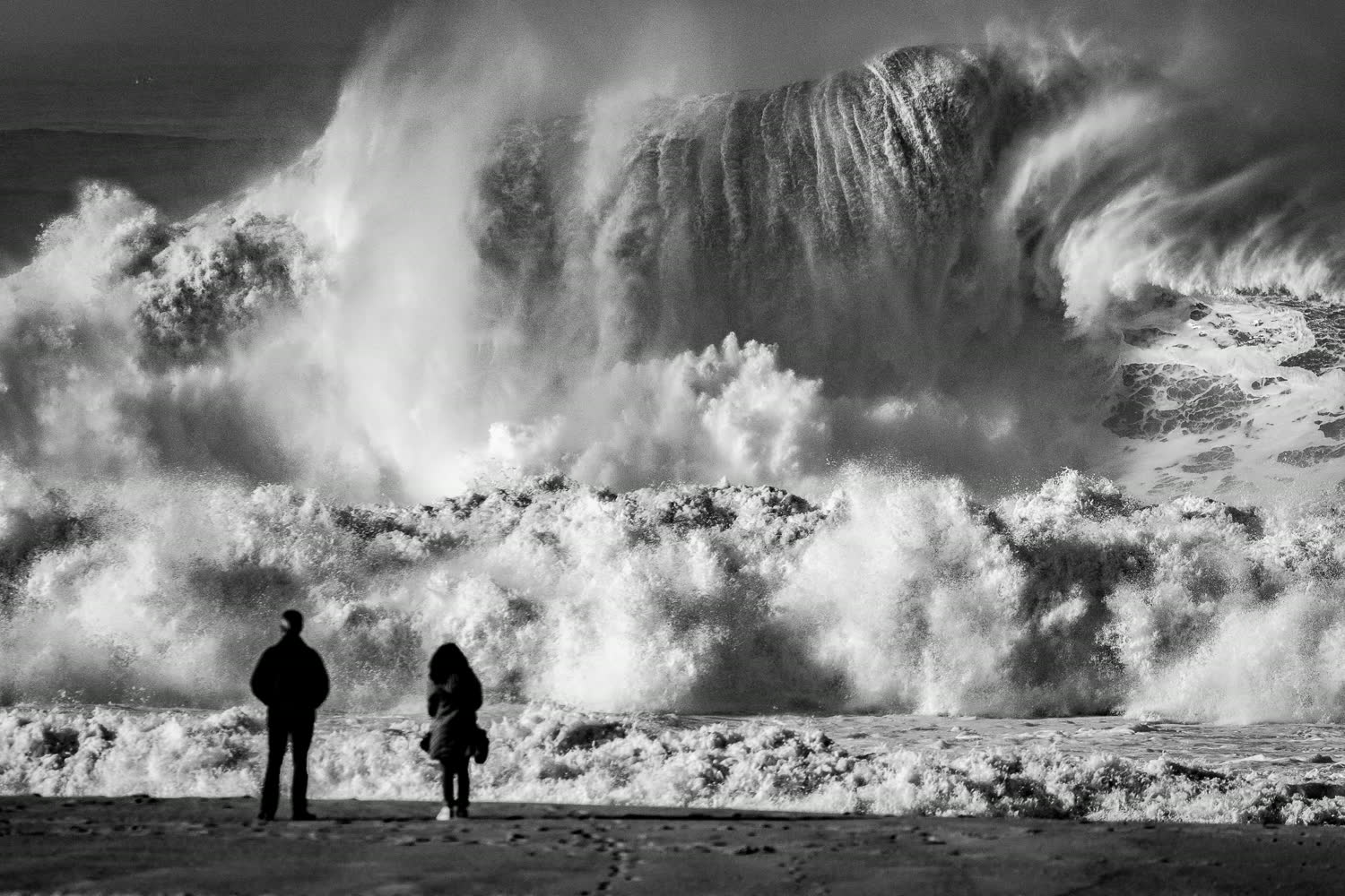 Vague géante et deux silhouettes sur la plage
